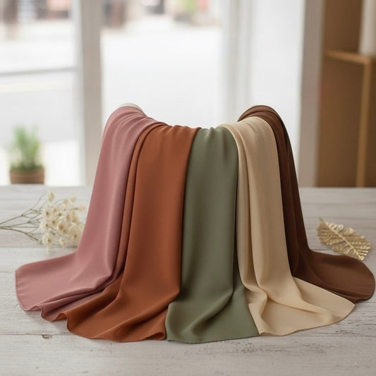 Five folded fabric swatches in pink, brown, green, beige, and brown on a light wooden surface.