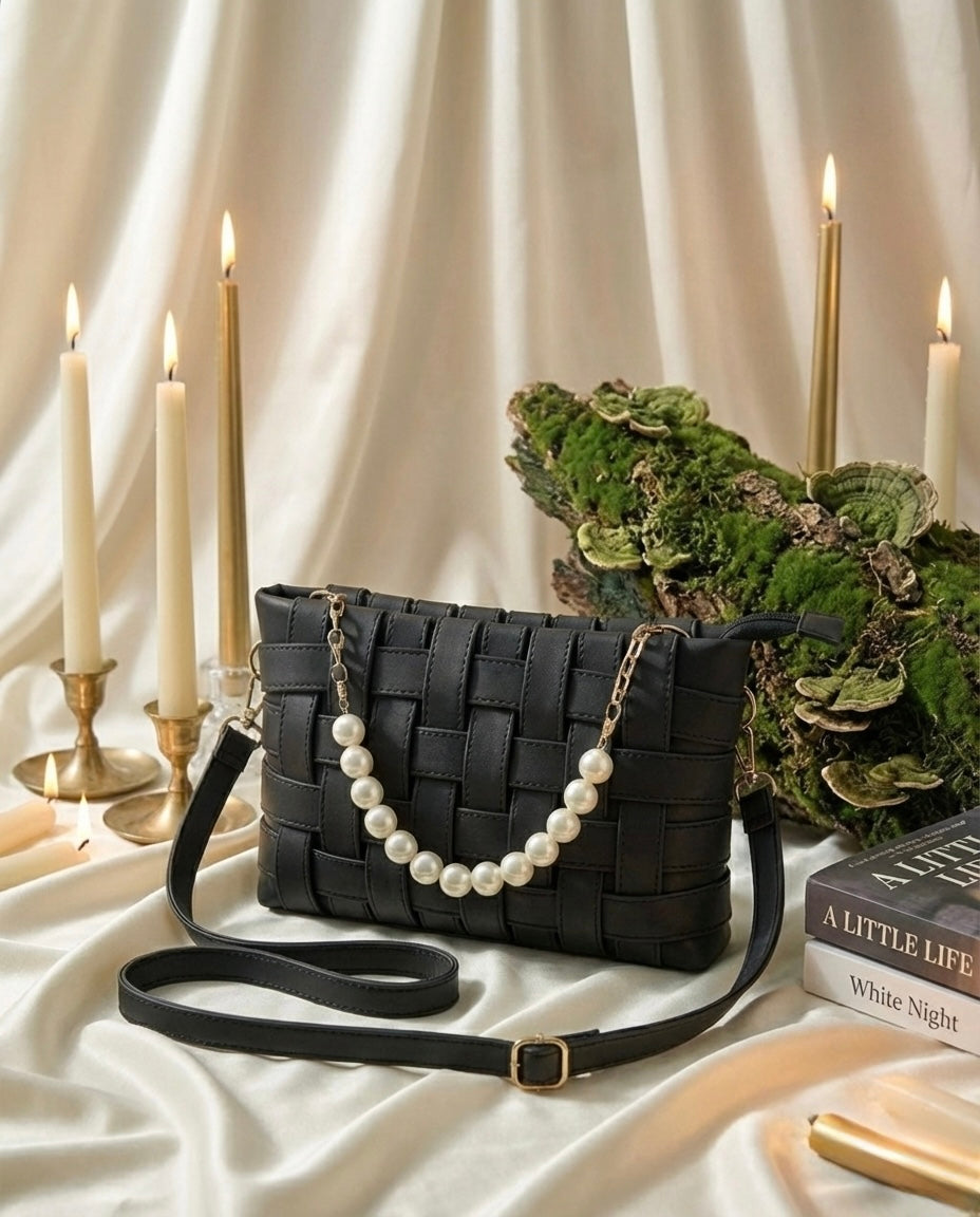 Black woven handbag with pearl strap on a white surface with candles and books.