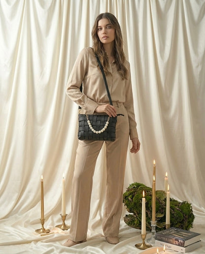 Woman holding a black handbag with white beads against a white curtain background