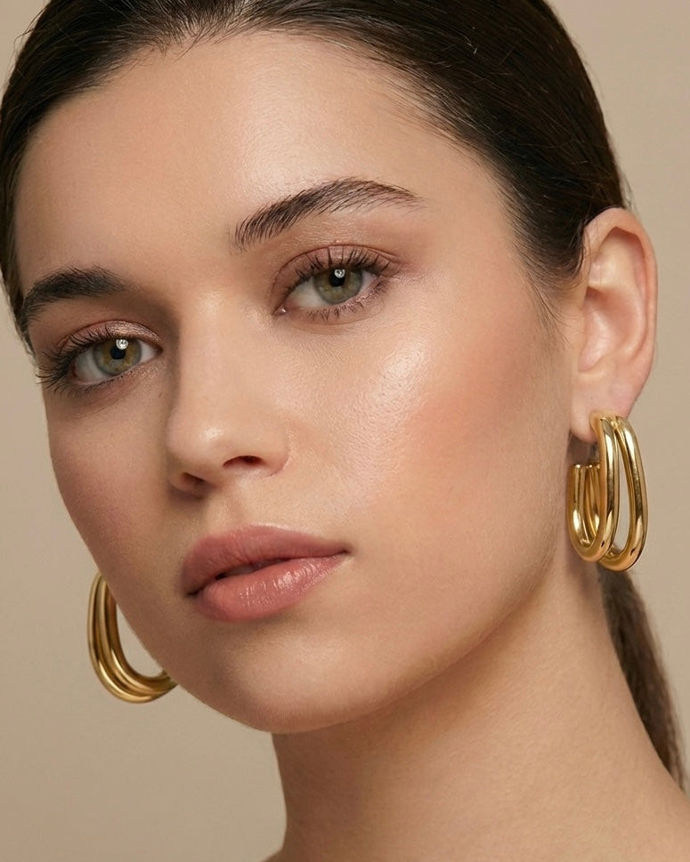 Close-up of a woman wearing gold hoop earrings against a neutral background