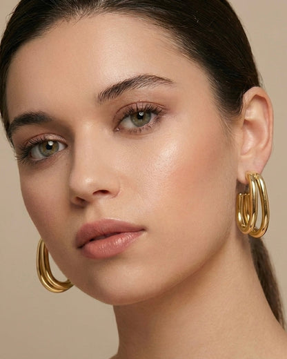 Close-up of a woman wearing gold hoop earrings against a neutral background