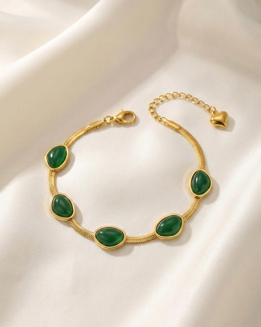 Gold bracelet with green stones on a white fabric background