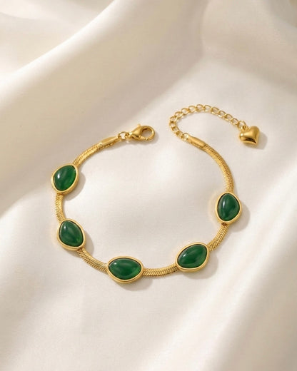 Gold bracelet with green stones on a white fabric background