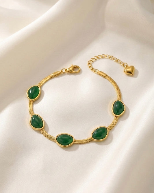 Gold bracelet with green stones on a white fabric background