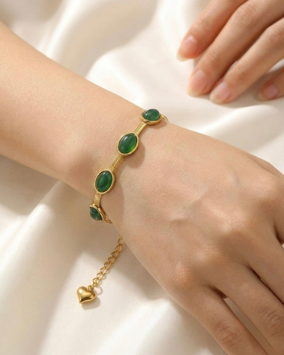 Gold bracelet with green gemstones on a wrist against a white background