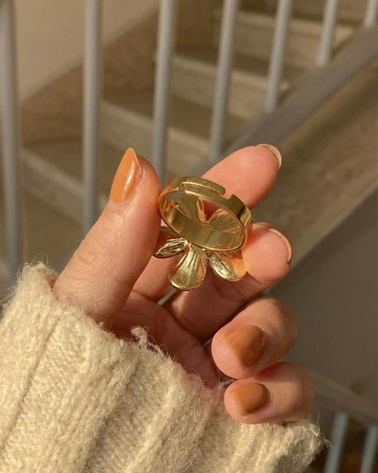 Gold ring held by a hand with beige nail polish, blurred background
