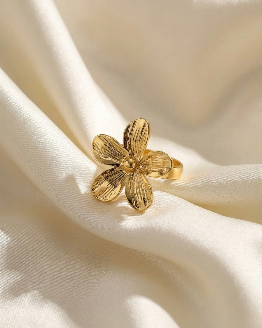 Gold flower-shaped ring on a soft beige fabric background