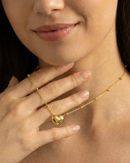 Close-up of a person wearing a gold necklace with a heart pendant.