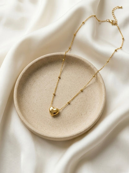 Gold necklace with a heart pendant on a beige plate against a white fabric background