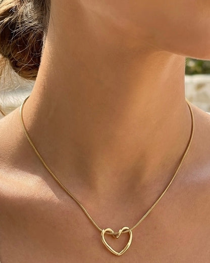 Gold heart-shaped necklace on a person's neck with a blurred background