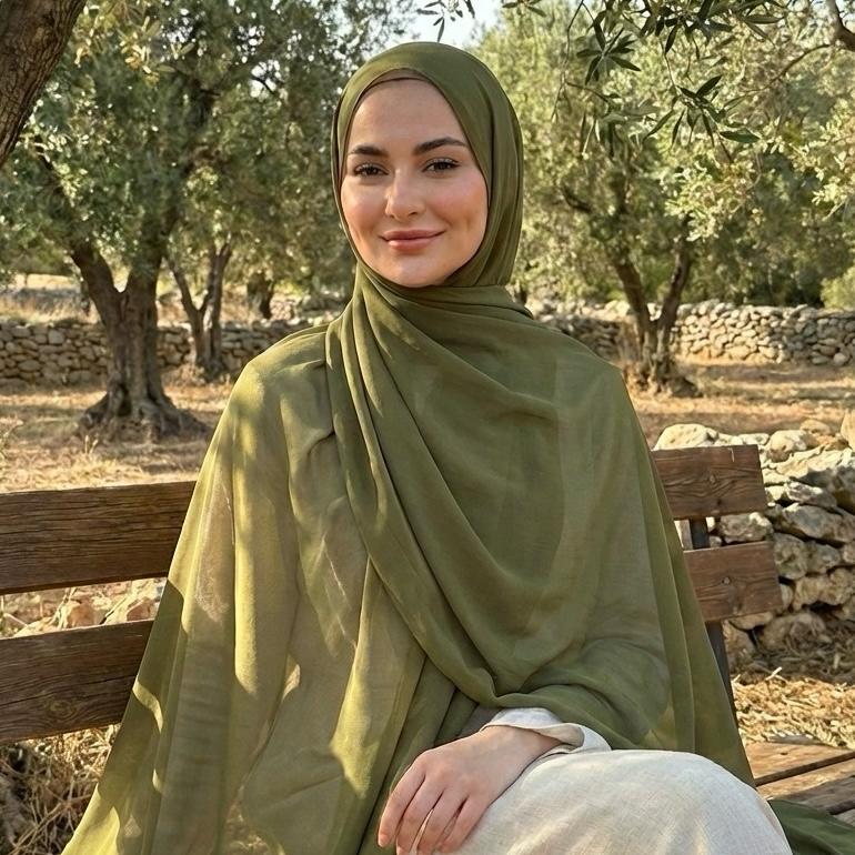 Woman in a olive green hijab sitting on a wooden bench outdoors.