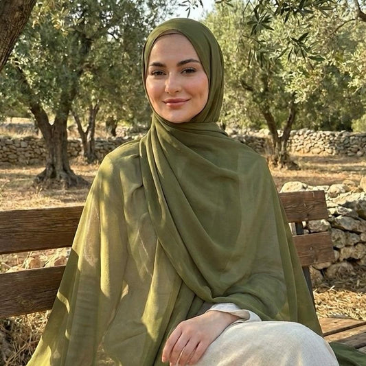 Woman in a olive green hijab sitting on a wooden bench outdoors.