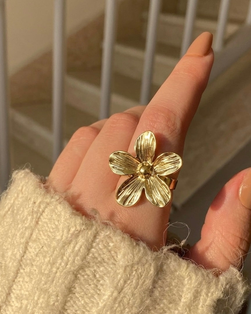 Gold flower-shaped ring on a finger with a neutral background